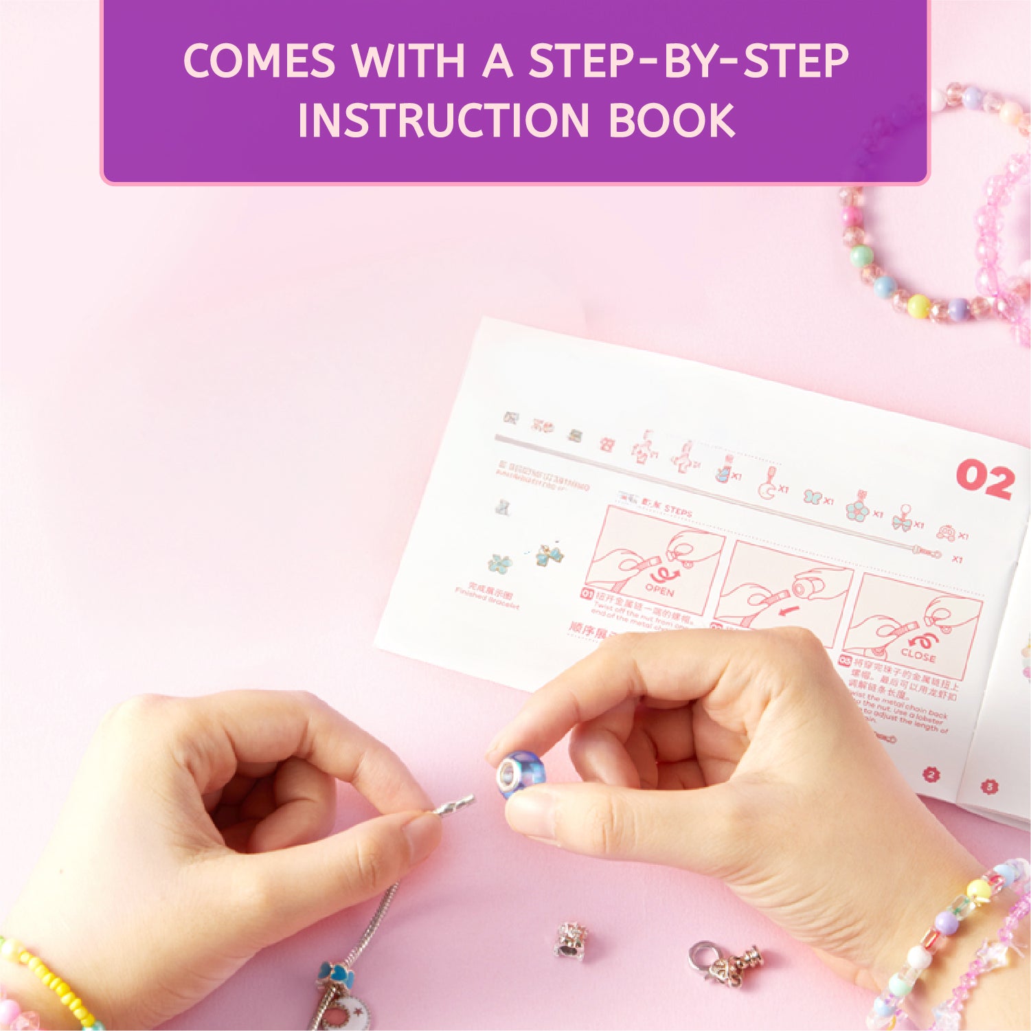 A person's hands are shown assembling a beaded charm on a pink surface, with a printed instruction sheet and a purple banner that reads 'COMES WITH A STEP-BY-STEP INSTRUCTION BOOK.'.