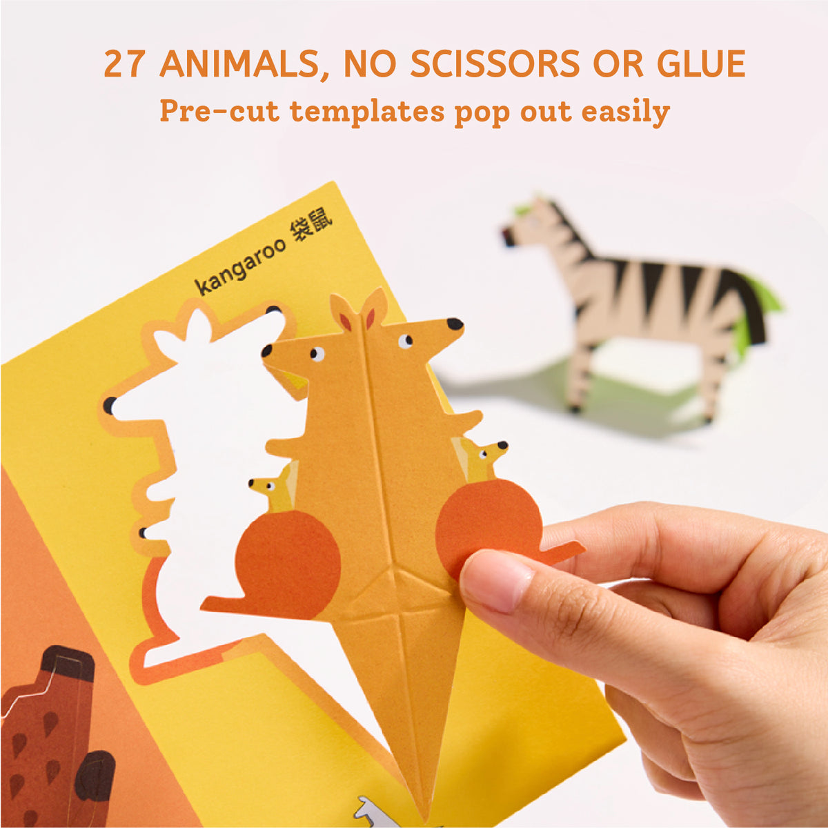A hand is holding a yellow pop-up animal craft card featuring a kangaroo, with other animal cards partially visible. Orange text at the top reads '27 ANIMALS, NO SCISSORS OR GLUE' and 'Pre-cut templates pop out easily.