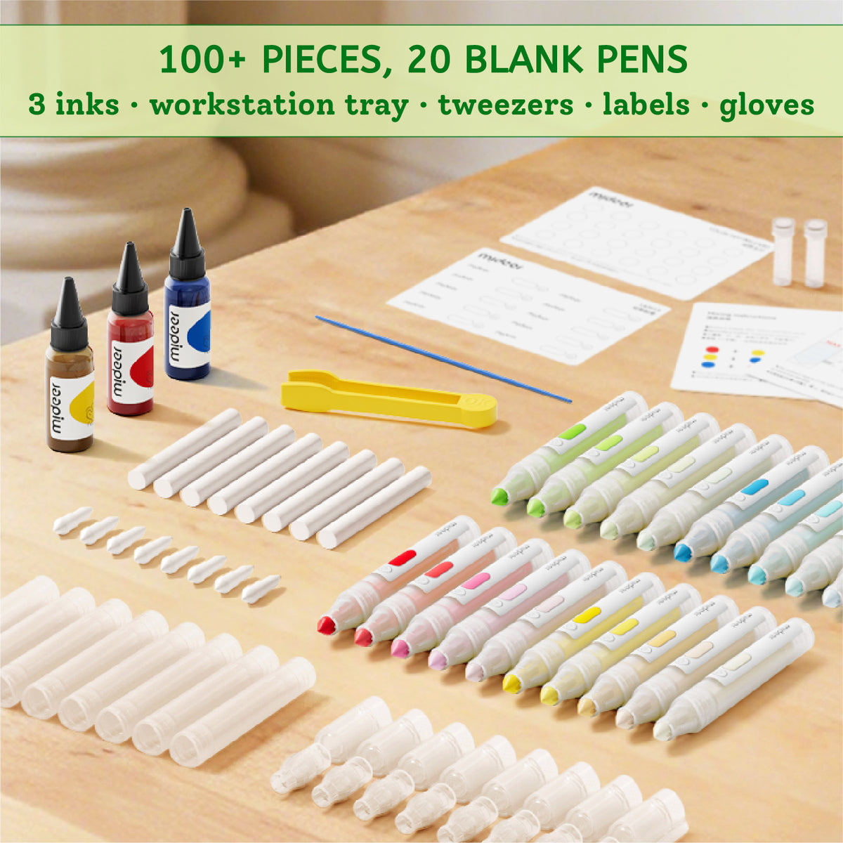 A tabletop display of a pen-making kit with many white blank pens, colored ink tips, small bottles of ink, tweezers, labels, gloves, and papers on a wooden surface. Text at the top reads '100+ PIECES, 20 BLANK PENS' and lists included items.