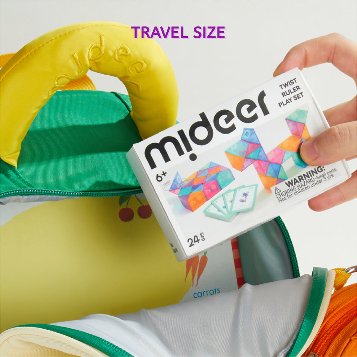 A hand holds a white Mideer twist-ruler play set box next to a colorful, travel-sized green and yellow bag, with the purple text 'TRAVEL SIZE' at the top.